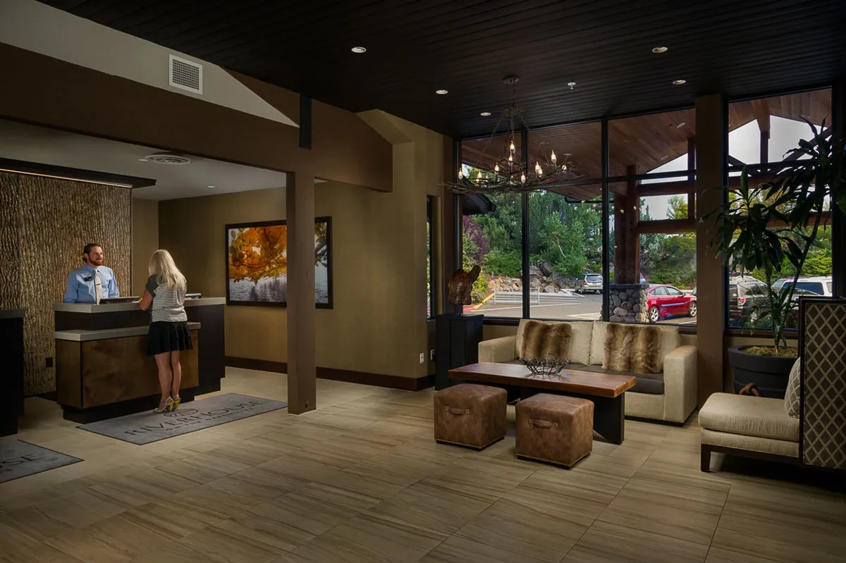 A bright and spacious reception area with a modern reception desk, tasteful artwork, a comfortable seating area, and large windows letting in natural light. The space feels welcoming and efficient, ideal for both business and leisure travelers.