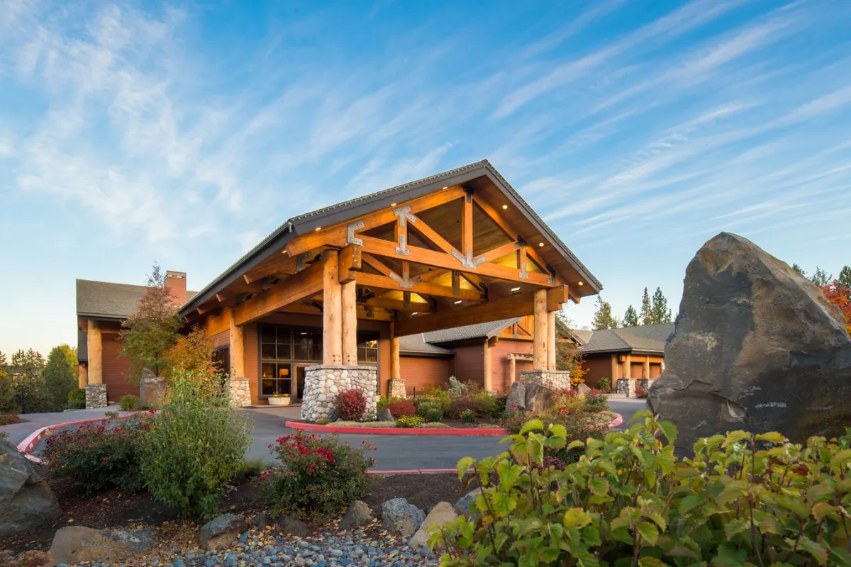 A warm, welcoming exterior shot of the property’s stone facade, wooden beams, manicured garden, and inviting entrance pathway. Guests are seen enjoying the garden and capturing the view, emphasizing the property’s connection with nature and relaxation.